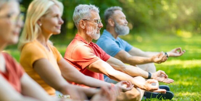 Group of Elderly Meditating Outdoors on Grass at Assisted Living Facility